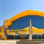 xterior view of Warner Bros. World Abu Dhabi, featuring a yellow and blue facade with the park's name and character figures.