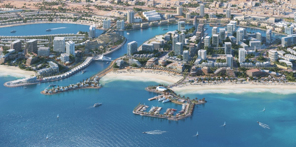 An aerial view of a modern waterfront city in Ras Al Khaimah, featuring high-rise buildings, sandy beaches, a marina, and luxury resorts along the coastline.