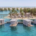 Aerial view of floating villas connected by boardwalks in turquoise water.