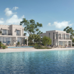 A modern two-story villa with a pool on a sandy beach, next to calm blue water.