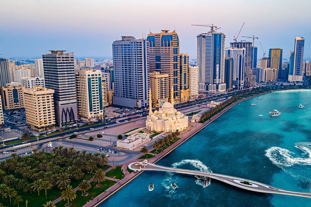 Aerial photograph of a city with tall buildings, a mosque with a large dome, and a turquoise body of water with a bridge and boats.
