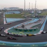 erial view of Formula 1 cars racing on the Yas Marina Circuit, with grandstands and the city skyline in the background.